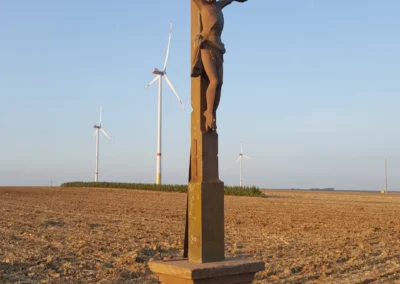Kreuz mit Feld und Windrädern im Hintergrund